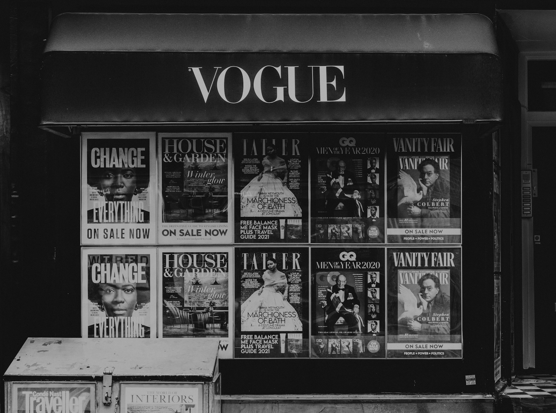 Storefront with multiple magazine covers displayed in a window. The magazines include titles such as Vogue, House & Garden, GQ, and Vanity Fair. The covers feature various themes and personalities, with a focus on fashion, lifestyle, and culture.